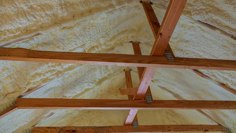 Wooden rafters coated with expanding spray foam insulation applied between them in attic space