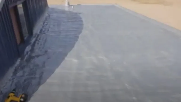 Flat commercial roof with a freshly applied dark gray roofing coating near a building edge in a sandy area