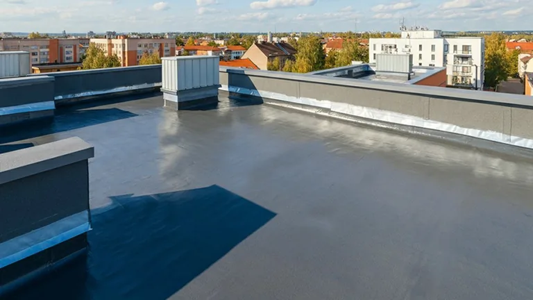Smooth, flat rooftop coated with SPF polyurethane under a partly cloudy sky in an urban area